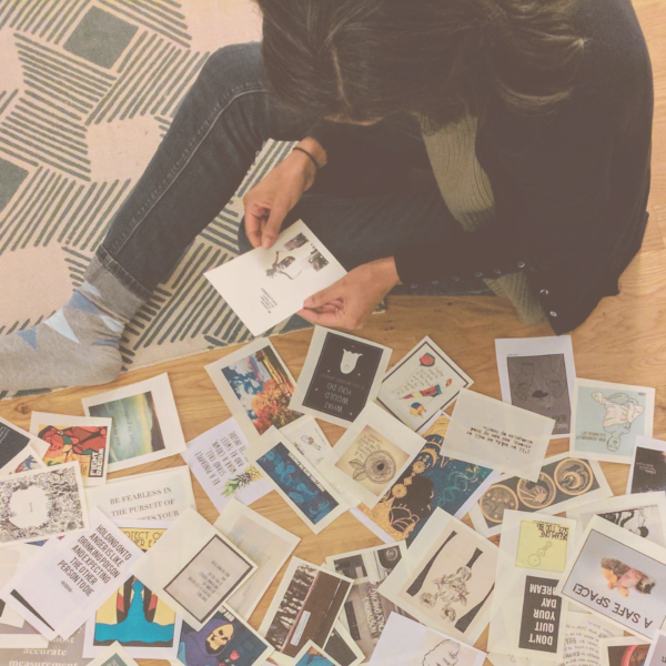 Photo from above of a woman of color sitting on the floor, looking through a pile of postcards and pictures